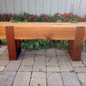 May include: A wooden bench with a natural wood finish and dark brown stained legs. The bench is made of solid wood and has a simple, modern design.