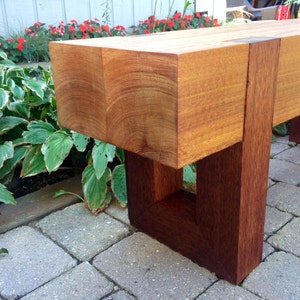 May include: A wooden bench with a natural wood finish and a dark brown stain. The bench has a simple design with a rectangular seat and four legs.