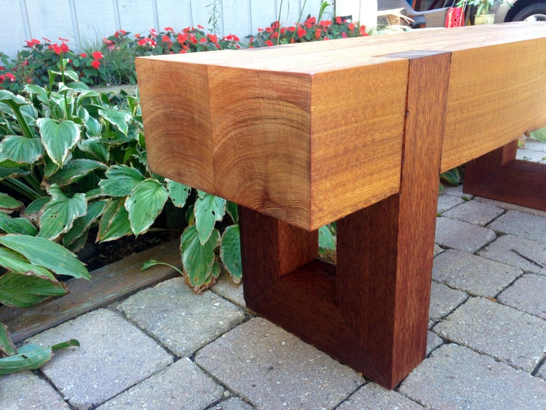 May include: A wooden bench with a natural wood finish and a dark brown stain. The bench has a simple design with a rectangular seat and four legs.