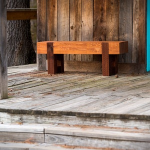 May include: A wooden bench with a natural finish sits on a wooden porch with a blue door in the background.