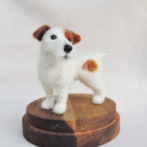 May include: A white and brown needle felted Jack Russell terrier dog figurine standing on a wooden base.