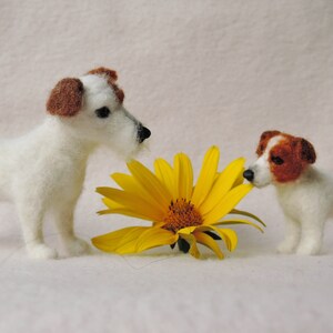 May include: Two white felt Jack Russell Terrier dogs with brown markings are sniffing a yellow felt sunflower.
