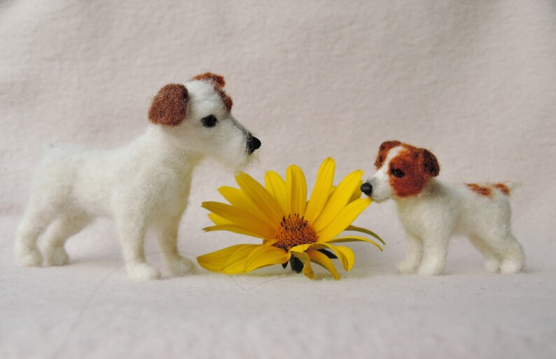 May include: Two white felt Jack Russell Terrier dogs with brown markings are sniffing a yellow felt sunflower.