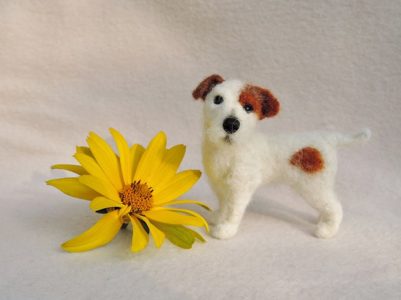 May include: A white and brown needle felted Jack Russell terrier dog figurine with a yellow flower.