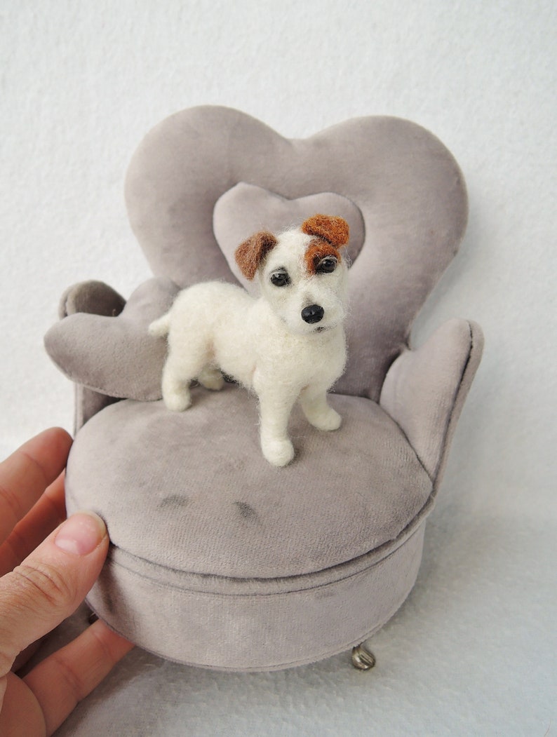 May include: A small white and brown needle felted Jack Russell Terrier dog sitting on a gray velvet heart-shaped chair.