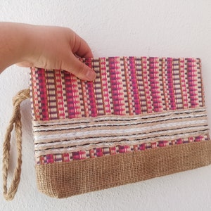May include: A pink, brown and white striped clutch bag with a brown jute bottom and a white braided trim. The bag has a brown rope handle.