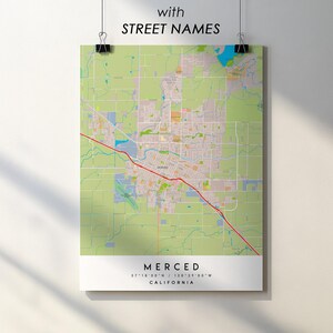 May include: A map of Merced, California, with street names, displayed on a poster. The map features a detailed layout of the city with a red highway cutting through the center. The poster includes the city's name, coordinates, and state.