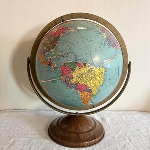 May include: A vintage globe with a light blue ocean and colorful continents. The globe is mounted on a wooden base with a brass-colored meridian ring. The globe is a decorative item, perfect for a study or office.