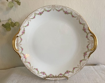May include: A white porcelain serving platter with gold trim and a delicate floral design. The platter has two handles and is perfect for serving a variety of dishes.