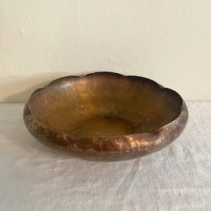 May include: A hammered copper bowl with a scalloped rim. The bowl has a warm, metallic brown color and a textured surface. The bowl is likely used for decorative purposes or serving.
