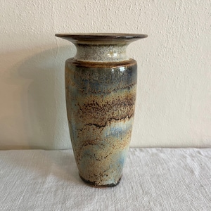 May include: A tall, ceramic vase with a wide, flat rim. The vase features a blend of colors, including brown, blue, and tan, creating a textured, earthy appearance. The vase is suitable for displaying flowers or as a decorative item.