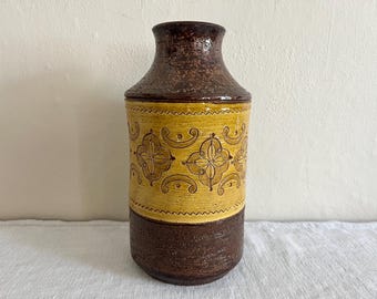 May include: A tall, decorative ceramic vase with a textured brown top and base. The middle section is yellow with a repeating brown floral pattern. The vase is approximately 12 inches tall.