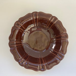 May include: A glossy, dark brown ceramic serving bowl with a scalloped rim. The bowl has a fluted design and a smooth, reflective surface. This decorative bowl is suitable for serving food.