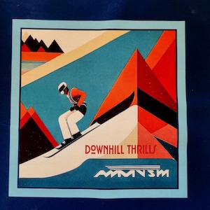 May include: A square print featuring a skier in orange and white attire, skiing down a snow-covered slope. The background includes geometric shapes in red, orange, and blue, with the words "DOWNHILL THRILLS" and a logo at the bottom. The print is framed in light blue.