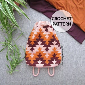 Könnte beinhalten: Ein gehäkelter Rucksack mit Kordelzug und einem geometrischen Muster in den Farben Hellrosa, Orange und Dunkelkastanienbraun. Die Tasche hat unten zwei hellrosa Träger und enthält den Text CROCHET PATTERN sowie @thestoryofamulberry.