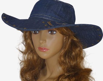 May include: A wide-brimmed denim hat with a dark blue wash and gold-colored metal accents. The hat has a wide brim and a crown with a slight curve.