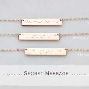 May include: Three rose gold bar necklaces with Morse code inscriptions. The necklaces are displayed on a white surface, with the phrases "I Love you", "Mother of an angel", and "I believe in me" written next to each necklace. The text "SECRET MESSAGE" is also visible.