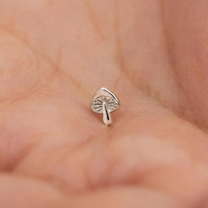 Peut inclure: Un petit charme en forme de champignon argenté avec un chapeau et une tige détaillés. Le charme est probablement en métal et a une finition polie. Le champignon est de taille miniature, idéal pour les bijoux ou autres créations.