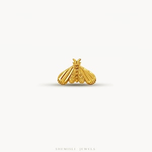 May include: A gold-coloured moth-shaped jewellery piece. The jewellery has detailed wings and body, with a textured surface. The piece is set against a white background. The brand name "SHEMISLI JEWELS" is at the bottom.