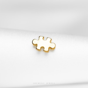 May include: A gold-coloured puzzle piece charm. The charm is a single piece of a jigsaw puzzle, with a smooth, polished surface. The charm is set against a white background. The text "SHEMISLI JEWELS" is at the bottom.