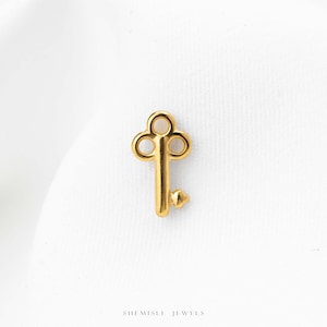 Peut inclure: Une petite breloque en métal doré en forme de clé ancienne avec un anneau arrondi et un panneton simple à la base. Le texte SHEMISLI JEWELS est imprimé en petites lettres capitales noires au centre en bas de l'image.