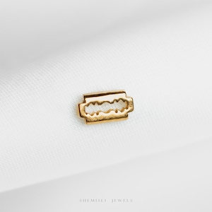 Peut inclure: Un petit charme en forme de lame de rasoir de couleur or. Le charme est posé sur un fond blanc. Le texte "SHEMISLI JEWELS" est au bas de l'image.