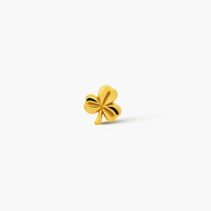 May include: A gold-coloured shamrock, a three-leaf clover, is shown against a white background. The clover has a detailed design with black accents. The image is well-lit, highlighting the clover's shape and texture.