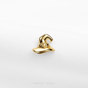 Peut inclure: Un charm en forme de chapeau de sorcière doré avec une boucle, sur fond blanc. Le charm est une représentation miniature d'un chapeau de sorcière, idéal pour les bijoux sur le thème d'Halloween ou fantastique.