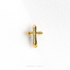 May include: A small, gold-coloured cross with a classic design. The cross is set against a white background, highlighting its polished surface and intricate details. The jewellery piece is a symbol of faith and spirituality.
