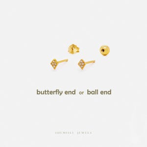 Peut inclure: Boucles d'oreilles dorées avec un motif en forme de losange, ornées de petites pierres transparentes. L'image montre deux boucles d'oreilles, un fermoir papillon et un fermoir boule. Le texte sur l'image indique "butterfly end or ball end".