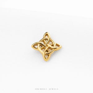 May include: A gold-toned metal charm featuring a four-pointed Celtic knot design with interlaced loops. The piece has a polished finish and a symmetrical shape. The text SHEMISLI JEWELS is printed in small black letters at the bottom of the frame.