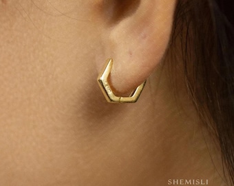 Può includere: Un orecchino a cerchio geometrico color oro. L'orecchino ha la forma di un esagono con chiusura a cerniera. L'orecchino è indossato sull'orecchio. Il marchio "SHEMISLI JEWELS" è visibile in basso a destra.