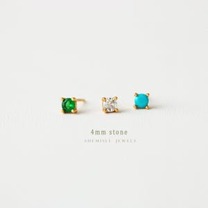 May include: Three gold stud earrings with 4mm stones: emerald green, clear, and turquoise. The earrings are displayed on a white background. The text "4mm stone" and "SHEMISLI JEWELS" are below the earrings.