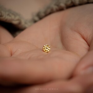 a close up of a person's hand holding a small gold bead