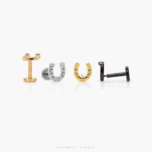May include: Four horseshoe-shaped earrings in gold, silver, and black. The earrings are displayed on a white background. The gold earring has a post and a horseshoe design. The silver earring has a horseshoe design. The black earring has a post and a horseshoe design.