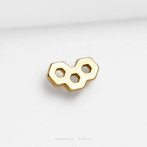 May include: A gold-coloured pendant with a honeycomb design. The pendant features three hexagonal shapes connected together, with a polished finish. The jewellery is displayed on a white background. The text "SHEMISLI JEWELS" is at the bottom.