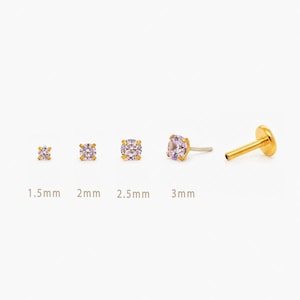 May include: A selection of gold-coloured stud earrings featuring light purple gemstones. The earrings are shown in sizes: 1.5mm, 2mm, 2.5mm, and 3mm. One earring is a labret stud. The gemstones are round or square-cut.