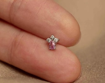 Può includere: Un piccolo orecchino argentato con una gemma rosa a forma di goccia al centro, circondata da tre gemme chiare più piccole. L'orecchino è progettato per un singolo piercing ed è mostrato su uno sfondo neutro.
