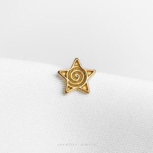 May include: A gold-coloured star-shaped stud earring with a spiral design in the centre. The earring is set against a white background. The jewellery piece is a small, detailed accessory.