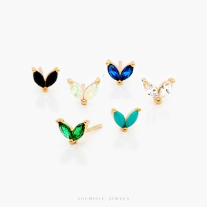 May include: A selection of gold stud earrings with leaf-shaped designs and various coloured gemstones. Gemstones include black, white, blue, clear, green, and turquoise. The earrings are presented against a white backdrop.