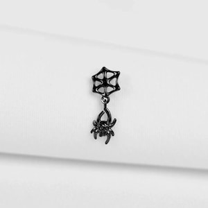 May include: A black spider web and spider charm. The charm features a spider web design at the top, connected by a small chain to a detailed spider pendant. The spider has eight legs and a detailed body.