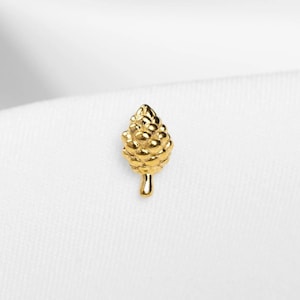Peut inclure: Boucle d'oreille unique en forme de pomme de pin dorée. Le bijou présente une surface texturée et détaillée, imitant les écailles d'une pomme de pin. L'arrière-plan est blanc.