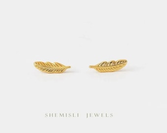 以下が含まれることがあります： 金色の羽のスタッドピアス2つ。ピアスは小さな羽のデザインが施されています。画像は白い背景で、下部に「SHEMISLI JEWELS」の文字があります。
