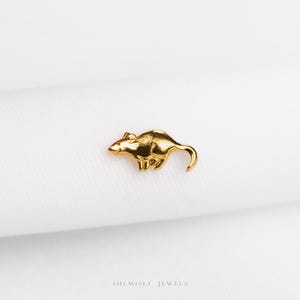 Peut inclure: Une petite figurine de rat dorée. Le rat est en position de course, avec sa queue courbée. La figurine est posée sur un fond blanc. Le texte "SHEMISLI JEWELS" est en bas.