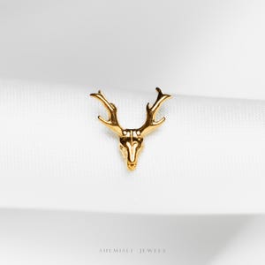May include: A gold-coloured deer head pendant with detailed antlers. The jewellery piece is set against a white background. The brand name "SHE MISLI JEWELS" is printed at the bottom of the image.