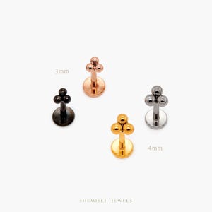 May include: Four lip piercing studs in black, rose gold, silver, and gold. Each stud features a cluster of three small spheres. The image includes the text "3mm" and "4mm" indicating the size of the studs. The brand name "SHEMISLI JEWELS" is at the bottom.