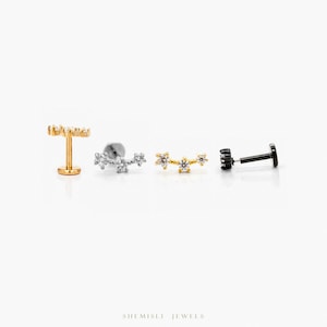 May include: Four stud earrings in different styles. The earrings are in gold, silver and black, and are decorated with small, sparkling gemstones. The earrings are displayed on a white surface.