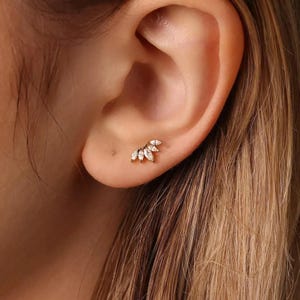 May include: A gold ear stud with five clear, marquise-cut gemstones. The earring is designed for the earlobe. The gemstones are arranged in a fan shape, creating a delicate and elegant appearance. The stud is a small piece of jewellery.