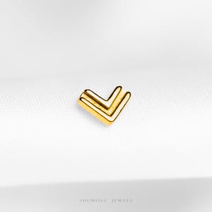 May include: A small, gold earring featuring a double chevron design. The earring has a bright, shiny gold finish and is set against a white backdrop. The words "SHEMISLI JEWELS" are visible at the bottom of the image.