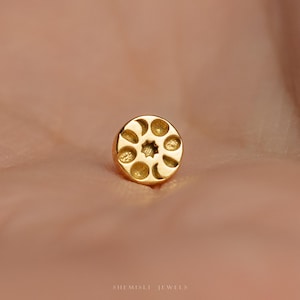 May include: A small, gold stud earring with a celestial design. The earring features a central star surrounded by circular and crescent moon shapes. The earring is shown on a light brown background. The text "SHEMISLI JEWELS" is at the bottom.